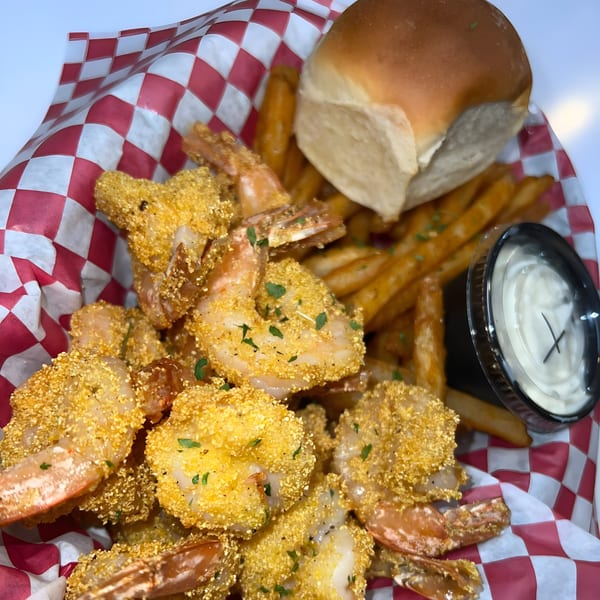 Royal Krabz fried shrimp and fries in a red and white checkered basket with a side of sauce.