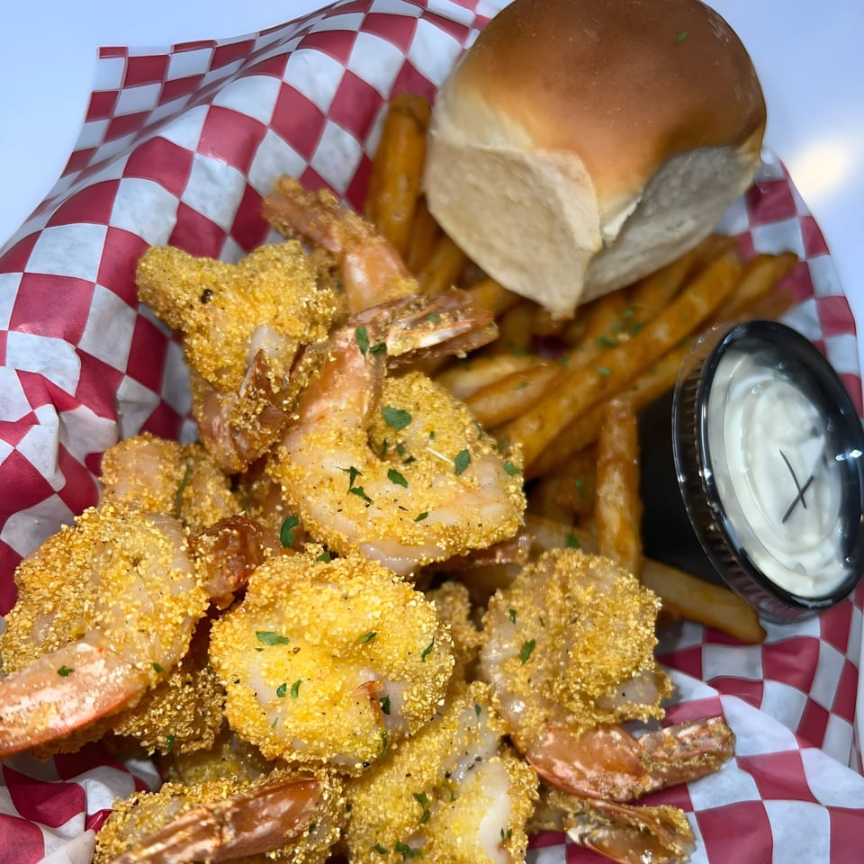 Royal Krabz fried shrimp and fries in a red and white checkered basket with a side of sauce.