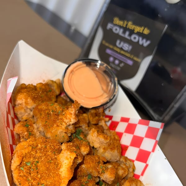 Royal Krabz fried seafood bites with seasoning and a side of dipping sauce in a paper tray.